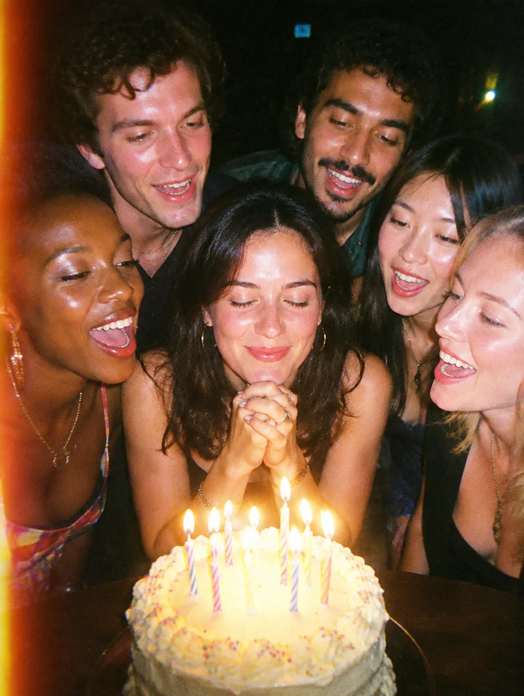 Friends cheering as a woman makes a wish over her cake